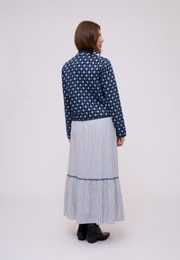 Giacca navy a fantasia floreale con maniche lunghe, abbinata a una gonna maxi a strisce e a balze. Entrambi i capi presentano un design rilassato.