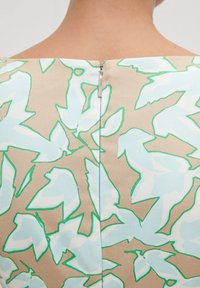 Bedrucktes Kleid mit beigem Grundton, das große blau-grüne Blattmuster zeigt, und einem dezenten Reißverschluss auf der Rückseite. Glatte Stoffstruktur.