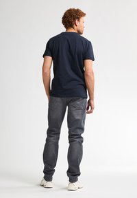 Námořnická modrá tričko s krátkým rukávem a šedé džíny, model otočený zády, volnočasový styl, tričko má kulatý výstřih, džíny jsou úzké.