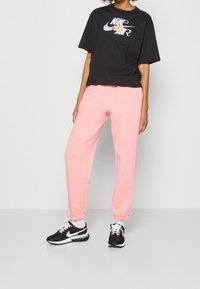 Svart kortärmad t-shirt med färgglogo "Nike Air" kombinerad med rosa sweatpants. Vita och svarta sneakers fulländar outfiten.