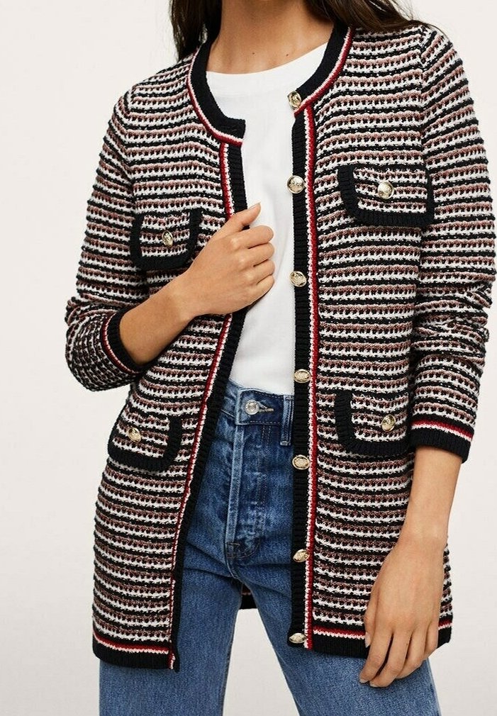 Femme portant un long cardigan en maille rayé avec des boutons dorés, un bord noir et des poches avant, par-dessus une chemise blanche et un jean bleu.