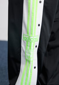 Fekete melegítő szett fehér és neon zöld függőleges csíkokkal. Kiváló minőségű hímzett Adidas logóval és patentos záródással az oldalukon.