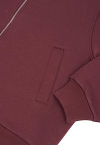 Brązowy rękaw kurtki na zamek z boczną kieszenią, ściągacz na mankiecie, widoczny zamek błyskawiczny oraz gładka tekstura tkaniny.