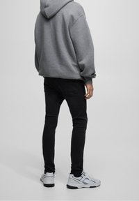 Sudadera gris con un ajuste relajado, jeans negros ajustados y zapatillas deportivas blancas con acentos grises. El material parece suave y casual.