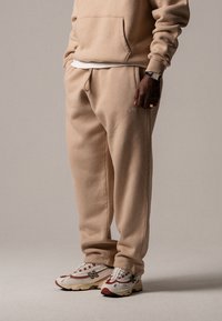 Beige sweatshirt og matchende joggebukser i myk stoff, med elastisk midje og sidelommer, paret med flerfargede sneakers.