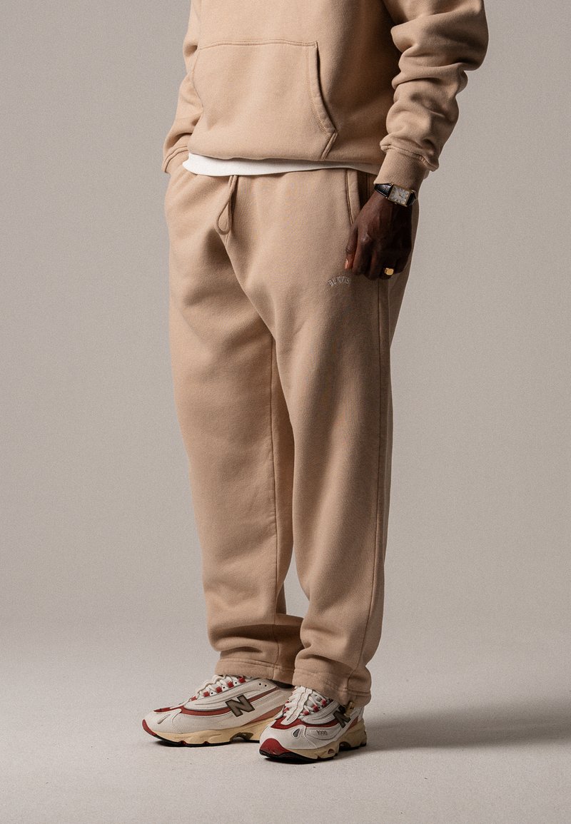 Beige Sweatshirt und passende Jogginghose aus weichem Material, mit elastischem Bund und seitlichen Taschen, kombiniert mit mehrfarbigen Sneakers.