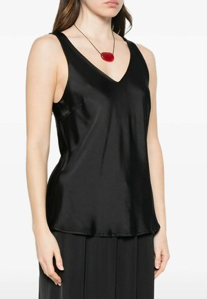 Donna che indossa un top nero in raso senza maniche con scollo a V e una collana con ciondolo ovale rosso su un sottile cordoncino nero, su sfondo bianco.