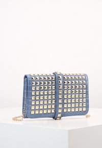 Modrá kabelka z umělé kůže s zlatými pyramidovými hroty, obdélníkový tvar, prošívaná textura, odnímatelný řetězový popruh a uzávěr na předním klopě.