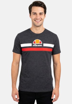 Homme souriant portant un t-shirt gris foncé avec des rayures horizontales blanches et rouges et un logo coloré "ellesse" sur la poitrine.