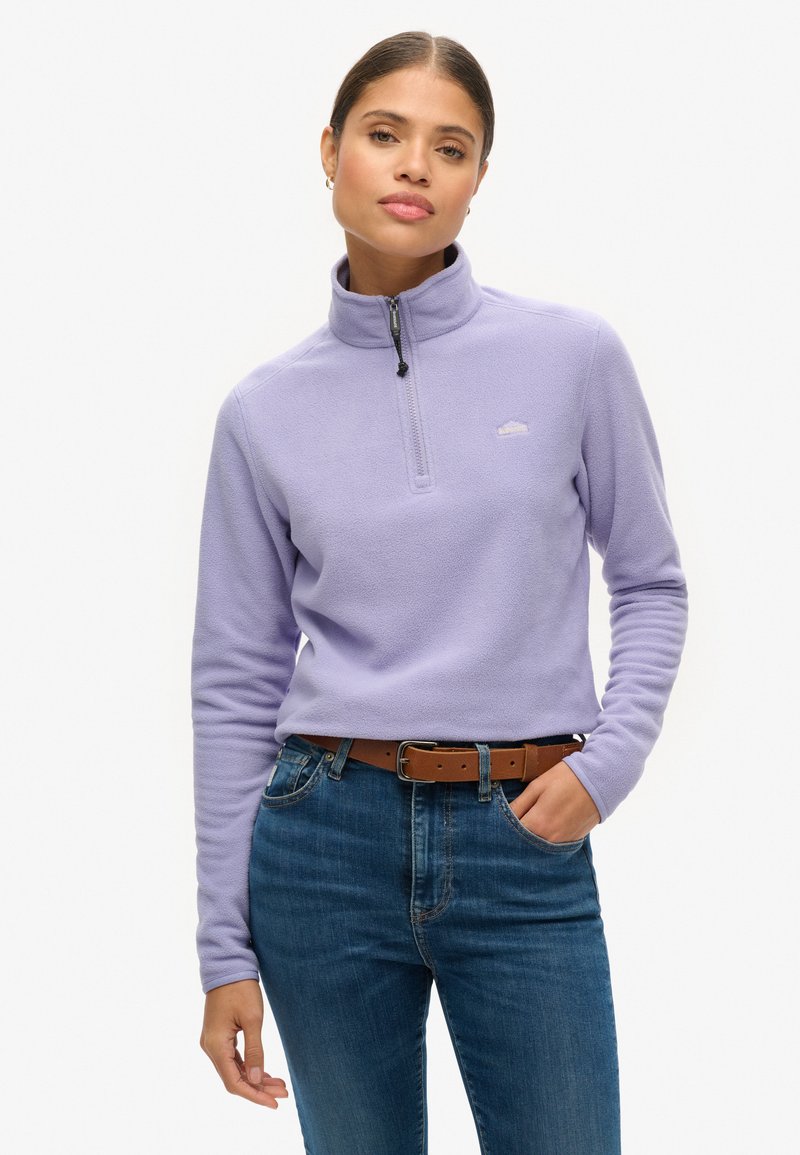 Lichtpaars fleece sweatshirt met een halflange ritssluiting en lange mouwen, voorzien van een subtiele logo op de borst, gecombineerd met blauwe spijkerbroek en een bruine riem.