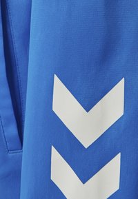 Blauwe stof met een gestructureerd oppervlak en een groot wit chevronpatroon in het midden. Het ontwerp is sportief met contrasterende kleuren.