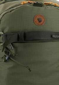 Grüner Rucksack aus strapazierfähigem Stoff mit Gittermuster, einem Leder-Logo-Patch, verstellbaren Gurten und einem Kordelzugverschluss.