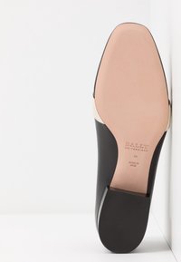 Talons de mocassin en cuir noir avec semelle beige clair portant la mention "Bally Switzerland", taille 38, fabriqué en Italie, photographiés sur fond blanc.