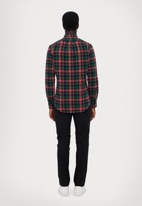 Camicia a quadri nera e rossa con maniche lunghe e colletto con bottoni, abbinata a pantaloni neri slim-fit e sneakers bianche. Vista posteriore mostrata.