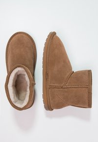 Brązowe zamszowe botki za kostkę z miękkim białym wykończeniem, okrągłym noskiem oraz teksturowaną gumową podeszwą zapewniającą przyczepność. Posiadają detal stębnowania wzdłuż szwów.