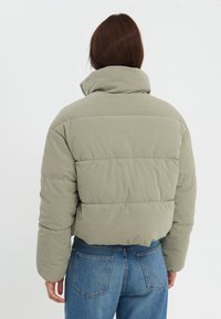 Kort puffjacka i texturerad olivgrön corduroy, med horisontella quiltade sektioner och hög krage, kombinerad med blå jeans.