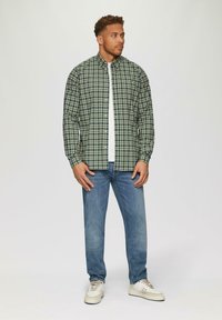 Zielona i granatowa koszula w kratę zapinana na guziki noszona na białej koszuli, w połączeniu z jasnoniebieskimi dżinsami i beżowymi trampkami. Charakteryzuje się długimi rękawami i standardowym kołnierzykiem.