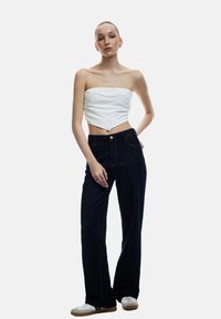 Witte strapless top gecombineerd met donkerblauwe wijde spijkerbroeken. De spijkerbroeken hebben een klassiek vijfzakken ontwerp en contrasterende stiksels. Witte schoenen maken de look compleet.