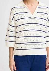 Strikpullover i creme med navy og blå vandrette striber. Har V-hals, korte ærmer og strukturerede detaljer med huller.