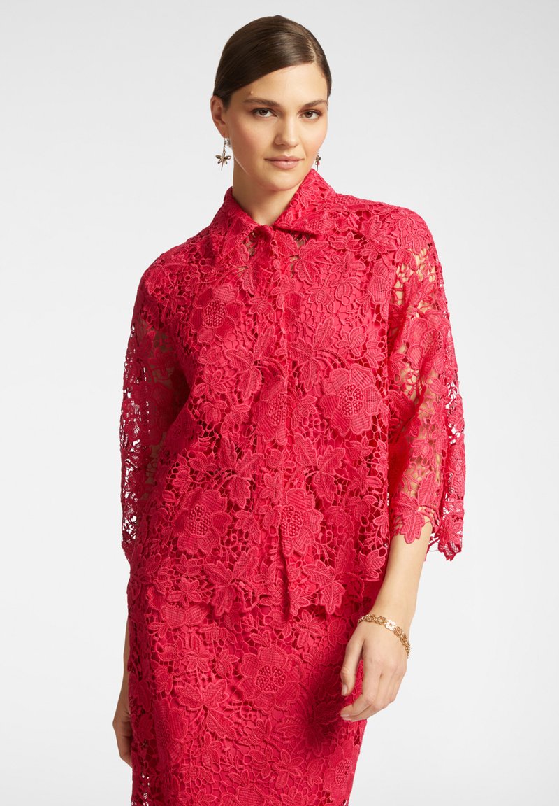 Abito rosso di pizzo con motivo floreale, collo a camicia e maniche a tre quarti. La texture è intricata con una finitura trasparente.