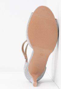 Chaussure à talon argenté avec un dessus texturé et un dos ouvert, dotée d'un talon fin et d'une semelle beige lisse avec des détails nervurés. Taille 38.