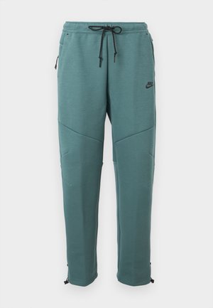 Pantalon de jogging Nike turquoise avec taille à cordon de serrage noir, poches latérales zippées, détails sur les panneaux aux genoux et jambes fuselées avec poignets réglables.