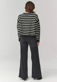Czarny i biały sweter w paski z dzianiny o teksturowanym wykończeniu, zestawiony z czarnymi spodniami dzwonami o wysokim stanie. Widoczny detal na mankiecie.
