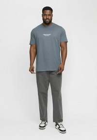 Grå bomulds t-shirt med rund hals og hvid "Original Studio" tekst. Sammen med antracitgrå bukser og sort-hvide sneakers.
