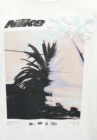 Λογότυπο Nike πάνω από ένα σχήμα με κουκκίδες που απεικονίζει φοίνικες και ήλιο με κυματιστές ακτίνες, συνοδευόμενο από μικρό κείμενο και σύμβολα μάρκας από κάτω.