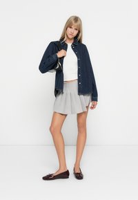 Denim shirt, white cropped top, gray pleated skirt, and burgundy flats. Simple design, soft textures, and contrasting colors. Black bag included.