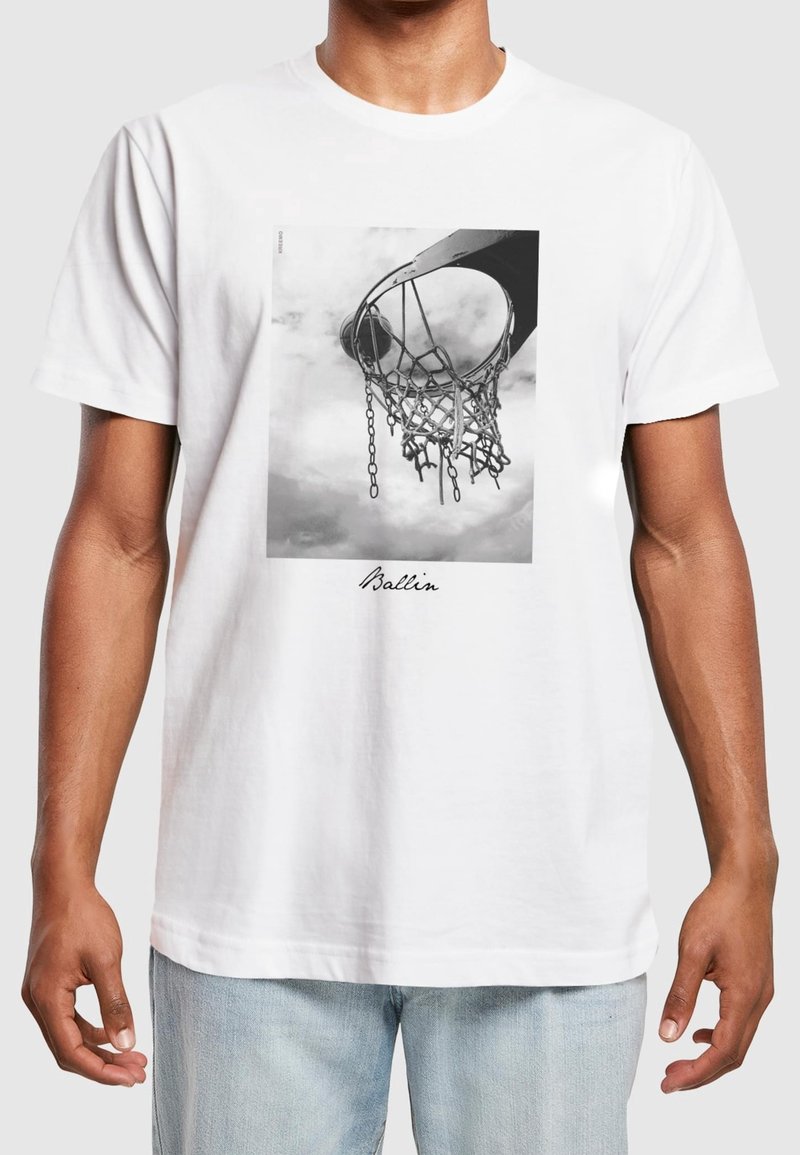 Homme portant un t-shirt blanc avec une photo en noir et blanc d'un panier de basket-ball et un filet avec le mot "Ballin" sous l'image.
