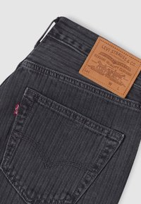 Υφασμα μαύρου τζιν με υφή ψαροκόκκαλου, με μία πίσω τσέπη, κόκκινη ετικέτα Levi's και καφέ δερμάτινο πλακέτα με στοιχεία εμπορικού σήματος.