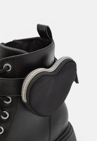 Zwarte leren enkelboot met een afgeronde zak en een zilveren rits aan de zijkant. Veters aanwezig met metalen oogjes.