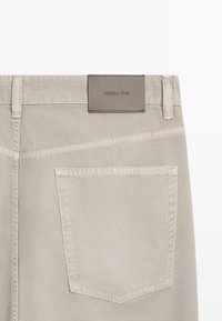 Vue arrière d'un pantalon beige montrant une grande poche arrière et une étiquette de marque en cuir cousue sur la ceinture indiquant "Massimo Dutti".