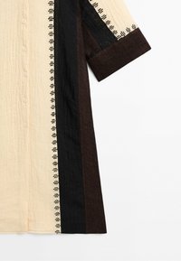 Buttoned shirt with vertical color blocks in beige, black, and brown, featuring patterned stitching along the edges of the beige sections.