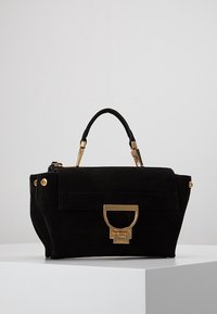 Mustassa mokkanahkakässärissä on jämäkkä muotoilu, kultaiset yksityiskohdat, yläkansi sekä erityinen suljenta. Pintamateriaali on sileä.