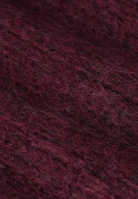 Tissu en laine bordeaux avec une surface texturée et duveteuse, présentant un mélange de fibres fines et grossières, créant une apparence chaleureuse.