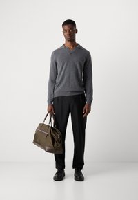 Gray knitted sweater with a V-neck, paired with black trousers. Brown and olive green bag with dual handles and zipper detail. Black shoes.