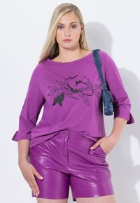 Paarse katoenen shirt met driekwart mouwen en een zwart florale print. Gecombineerd met glanzende paarse neplederen short.