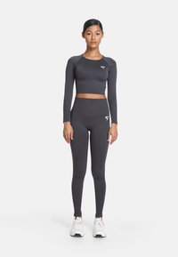 Tmavošedý crop top a legíny s vysokým pásom vyrobené z priliehavého, elastického materiálu. Obsahujú logo na vrchu a hladkú textúru. Bíle tenisky.