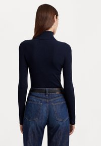 Pull encolure roulée côtelé marine à manches longues, associé à un jean en denim bleu taille haute avec un design de poche classique.