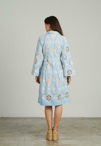 Blaues Baumwollkleid mit Blatt- und Blumen-Spitzenmustern, langen Glockenärmeln und einem Taillengürtel. Getragen mit beige Espadrille-Plateauschuhen.