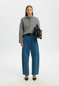 Halli pika varrukaga polo-särgi ja kõrge vöökohaga, laiade sääreosadega siniste teksapükstega komplekt. Modell hoiab musta kotti, mille küljes on triibuline sall.