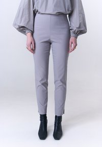 Hellgraue, eng anliegende Hose mit hohem Bund und seitlichen Schlitzen am Saum, kombiniert mit schwarzen Stiefeletten. Glatte Textur, minimalistisches Design.