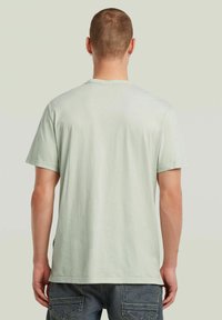 Maglietta verde chiaro a maniche corte, realizzata in tessuto morbido, con collo rotondo e vestibilità rilassata. Vista posteriore con superficie liscia e senza motivi.