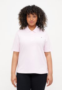 Hele roosa polo särk lühikeste varrukatega ja klassikalise kaelusega, millel on nööbiplakk ja väike logodetail rinnal.
