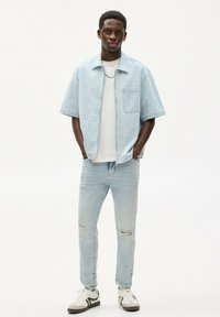 Světle modrá košile s krátkým rukávem z texturované tkaniny, spárovaná s opranými světle modrými džíny a bílými teniskami s černými akcenty.