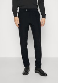 Fekete, sima anyagból készült, szabott nadrág, gombos zárással, övhurkokkal és slim fit fazonnal. Fekete cipővel párosítva.