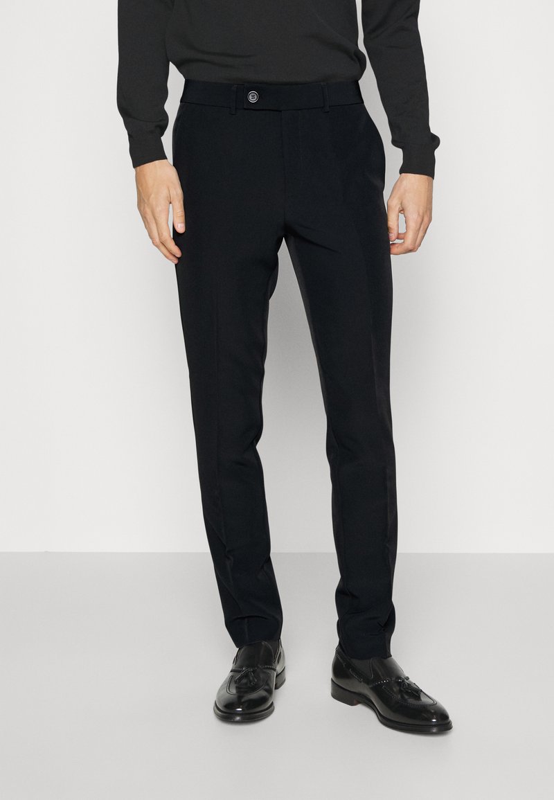 Fekete, sima anyagból készült, szabott nadrág, gombos zárással, övhurkokkal és slim fit fazonnal. Fekete cipővel párosítva.