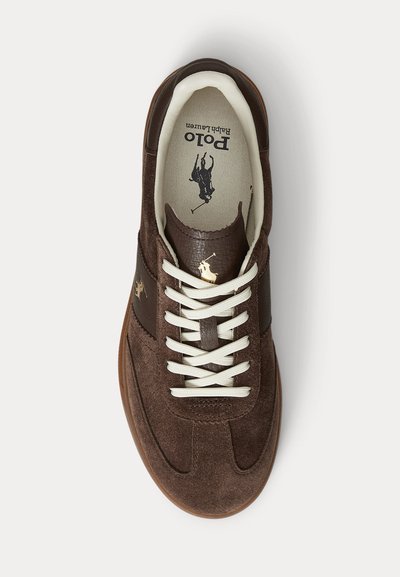 Rudas zomšinis sportbačiai su baltais raišteliais, tarp jų pusėje ir vidinėje pado pusėje - polo žaidėjo ant arklio logotipas, matoma gumos padų dalis.